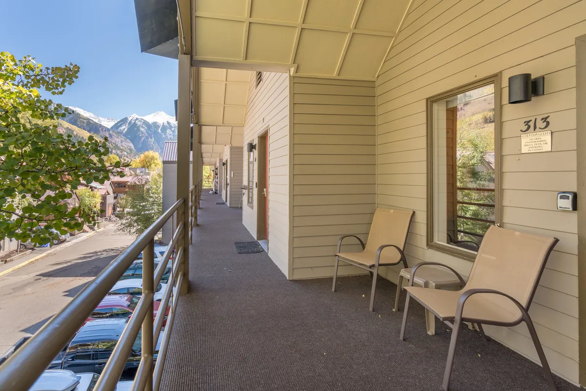 This exterior image features a tranquil balcony seating area with sweeping mountain views visible in the background. The entrance doors and outdoor seating invite relaxation and morning rituals, like sipping coffee while gazing at the scenery.