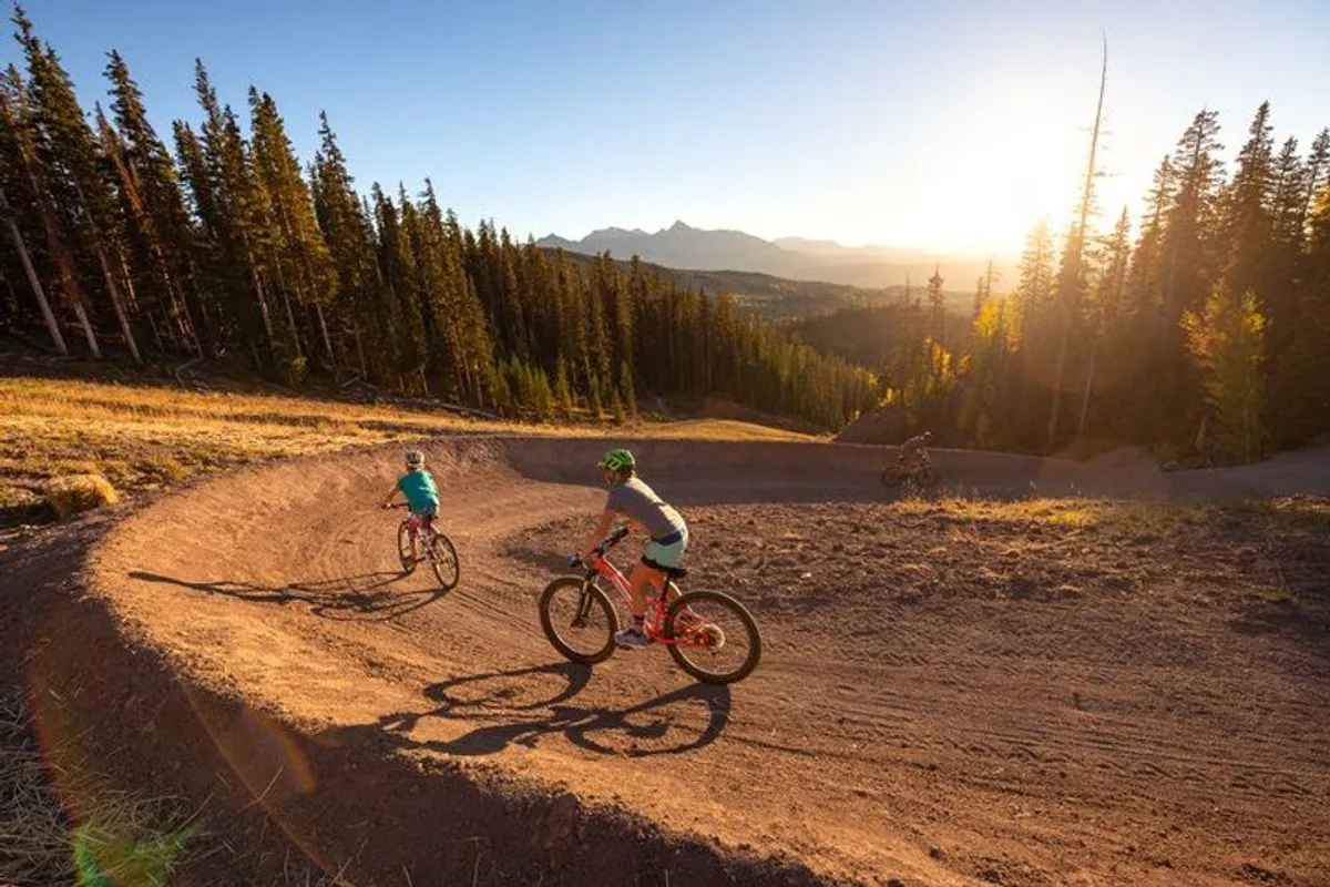 An exhilarating view of bikers riding along a winding trail set against a breathtaking mountain backdrop. The natural terrain and expansive views evoke a sense of adventure and access to scenic outdoor experiences.