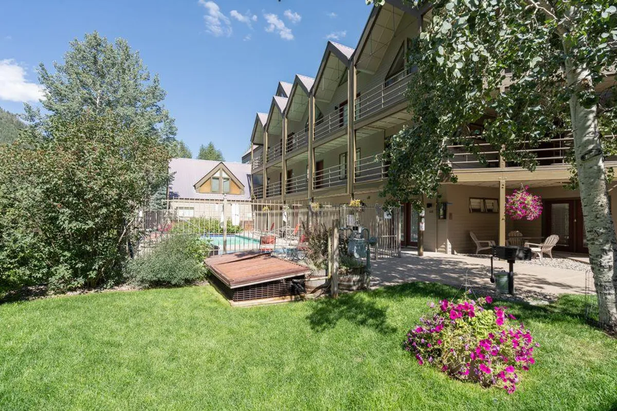 A cheerful outdoor swimming pool surrounded by balconies, vibrant flower beds, and lush green grass. The scene exudes a sense of relaxation and fun, with plenty of space for socializing or sunbathing. The pool is an obvious focal point and is flanked by inviting communal areas that likely host guests enjoying warm days.