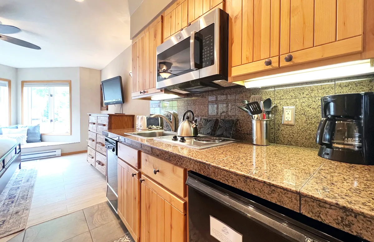 A compact yet inviting kitchenette with granite countertops, wood cabinets, kitchen appliances, and a cozy window seating area. The scene suggests both the convenience and warmth of preparing and enjoying meals in a connected space.