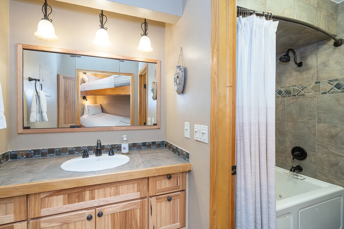 This serene interior image centers on a sink with wooden cabinetry and a large mirror, with the shower area visible in the background. The color palette and layout exude calm, making the space ideal for unwinding after a day of adventure. The scene suggests an atmosphere of self-care and relaxation, complementing the narrative of soothing tired muscles.