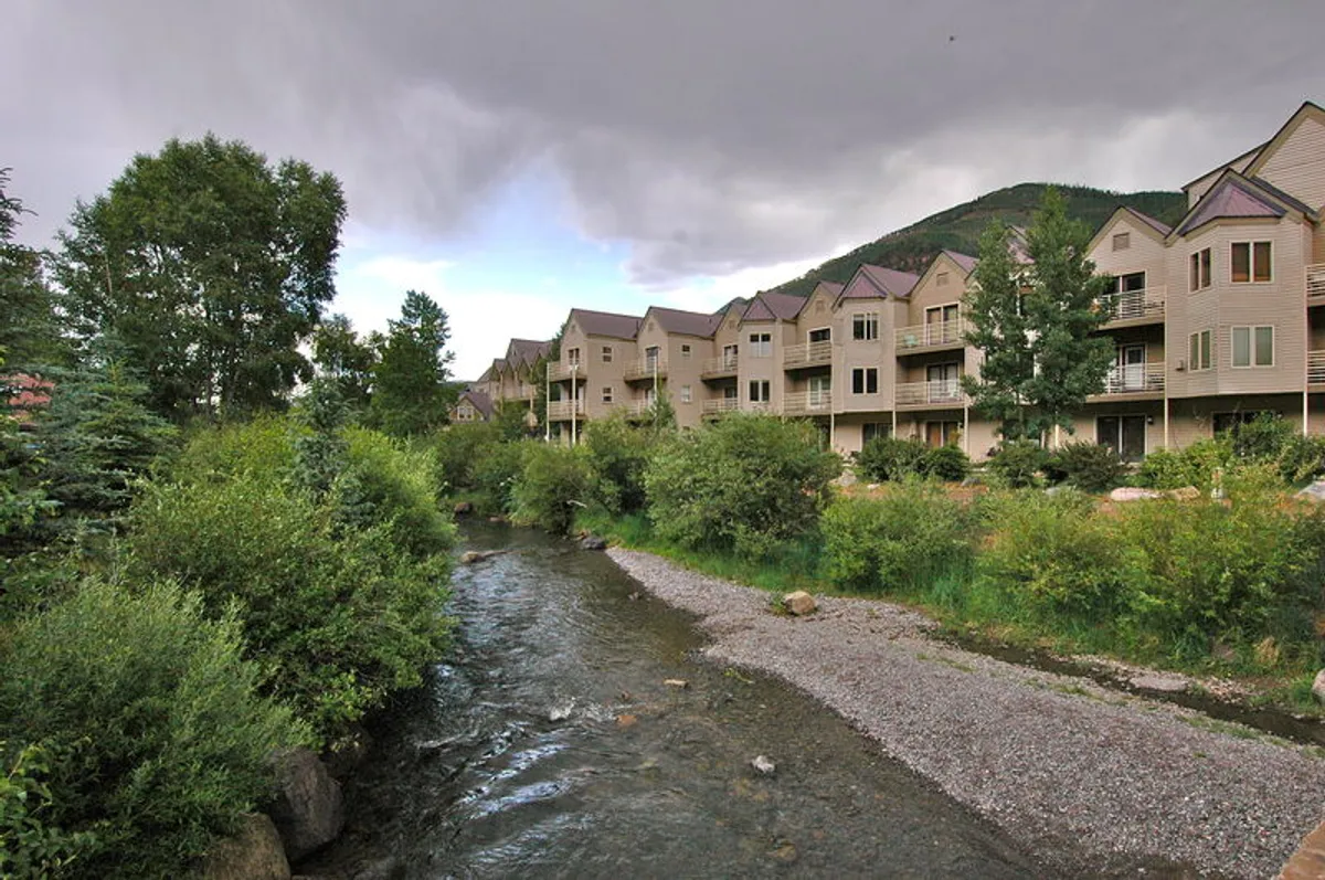 A peaceful stream winds its way alongside lush greenery, with buildings in the background. The scene suggests easy access to the river trail and opportunities for tranquil walks or peaceful moments by the water.