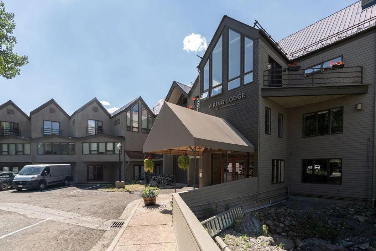 This image shows the exterior entrance of Viking Lodge, featuring a prominent sign, an inviting awning, large windows, and some landscaped greenery. People can be seen checking in and relaxing outside, suggesting a friendly and welcoming environment right in town.