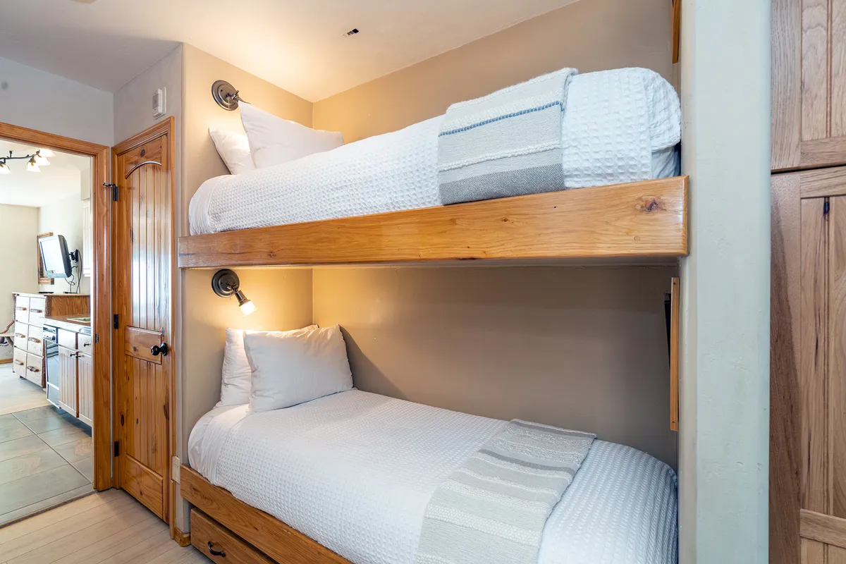 A set of built-in bunk beds with wall-mounted reading lights and textured bedding. The playful yet cozy design makes the sleeping space inviting for children and smaller adults. The surrounding decor is simple, suggesting a safe and comfortable nook for restful or story-filled evenings.
